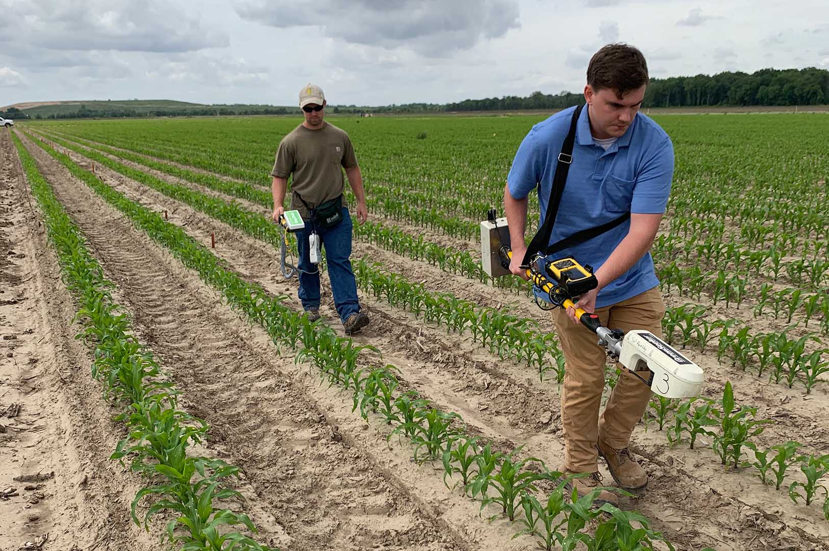 Former graduate student Joey Williams (left) uses a crop circle sensor while Camden Oglesby, graduate student, uses a green seeker sensor. The sensors are collecting corn reflectance data. (Photo submitted)