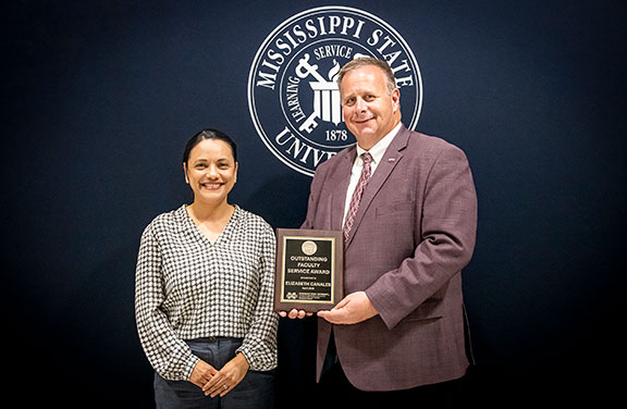 Elizabeth Canales with the dean in front of a black backdrop with university seal