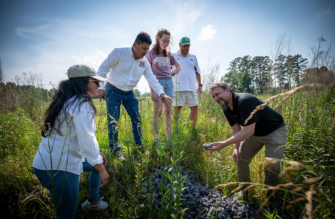 Tim Schauwecker, right, and John Ramirez-Avila, second from left, show a piece of slag to students in the field. 